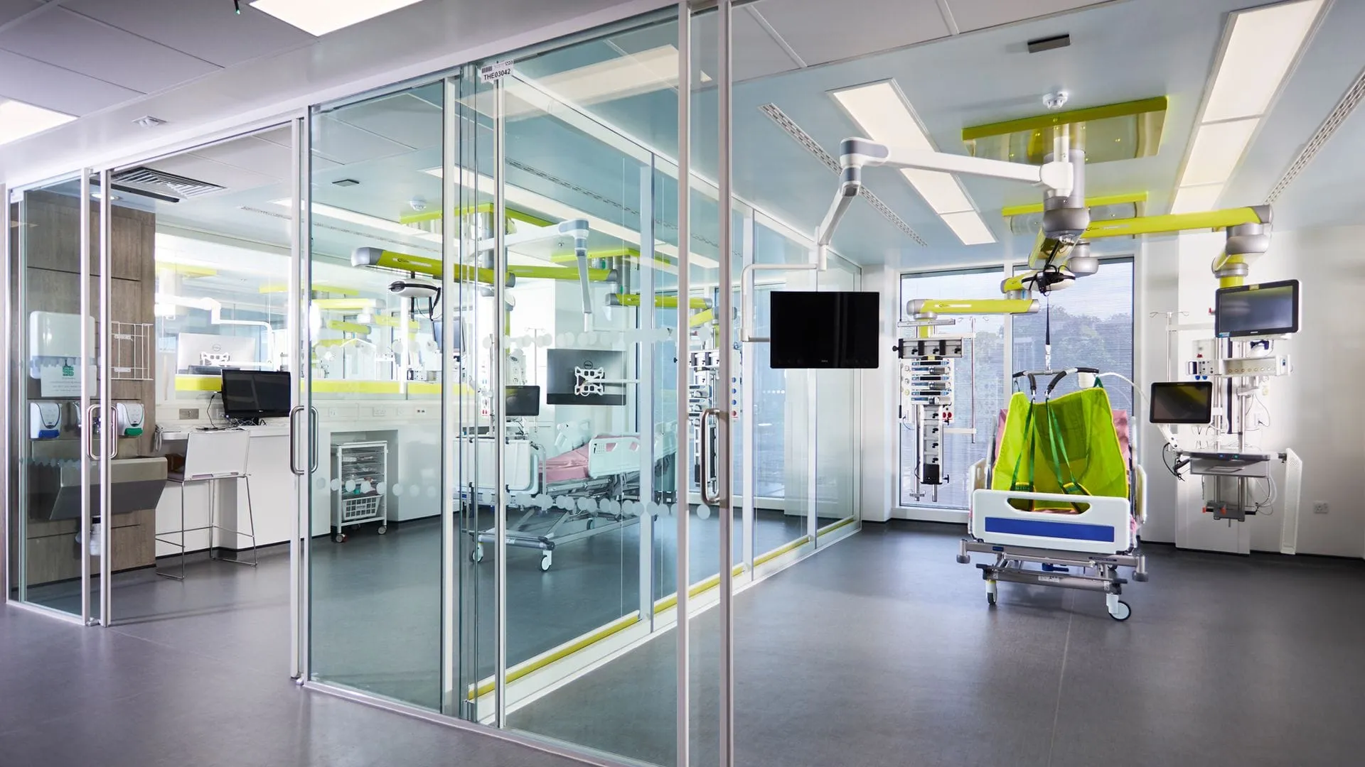 Modernes Krankenzimmer mit Glastrennwand, medizinischen Geräten, Patientenbett und grüner Akzentbeleuchtung