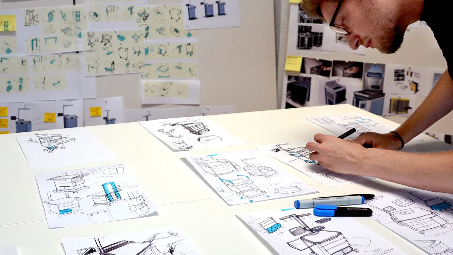 Designer skizziert Medizinproduktkonzepte an einem Tisch umgeben von detaillierten Industriedesign-Zeichnungen