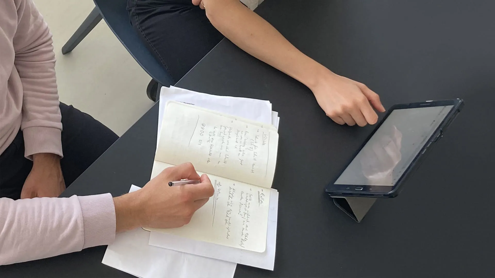 Zwei Personen sichten handschriftliche Notizen und ein Tablet während einer summativen Evaluationssitzung