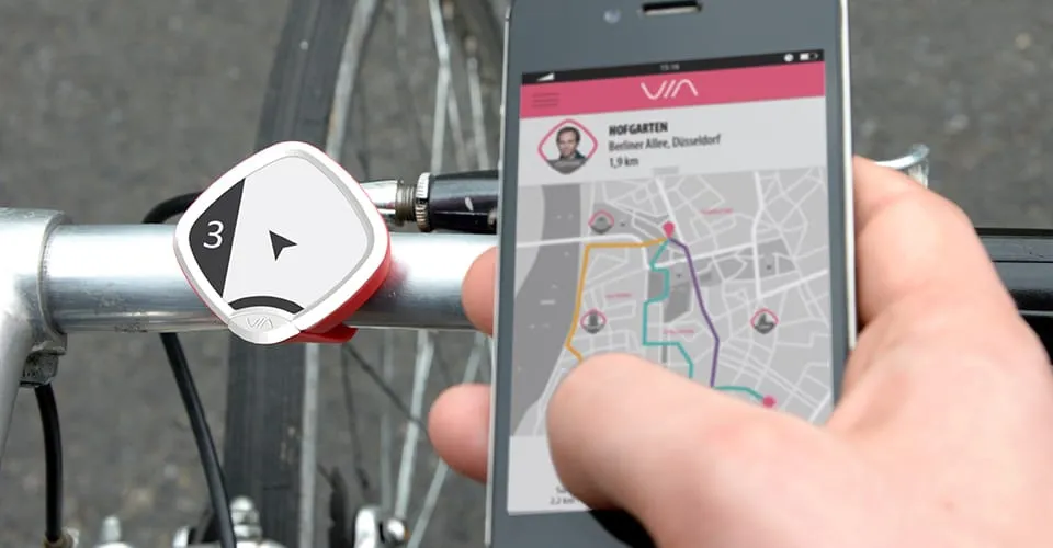 VIA Navigationsgerät am Fahrradlenker befestigt neben Smartphone mit VIA-App und Stadtkartenansicht