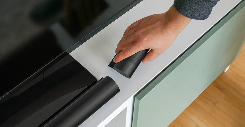 Hand greift einen zylindrischen AIRO Bluetooth-Satellitenlautsprecher vom TV-Schrank