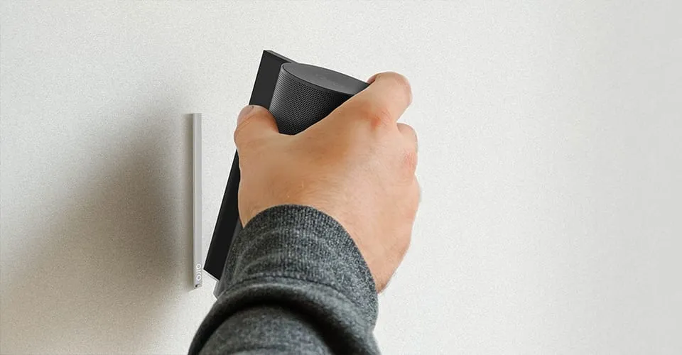 Hand hält einen AIRO Bluetooth-Lautsprecher an eine wandmontierte Dockinghalterung