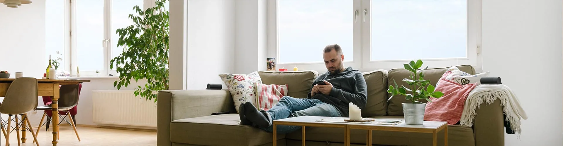 Mann entspannt auf dem Sofa mit Smartphone und AIRO Soundbar in einem hellen Wohnzimmer