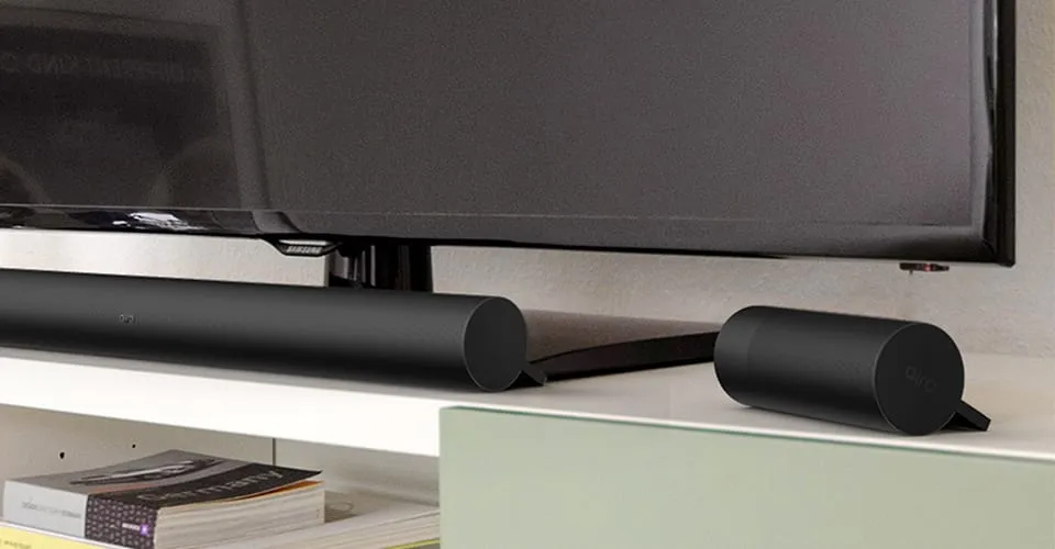 AIRO Soundbar und Bluetooth-Satellitenlautsprecher auf einem TV-Schrank unter einem Flachbildfernseher
