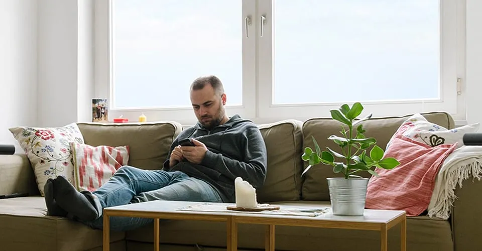 Mann entspannt auf dem Sofa und steuert das AIRO Soundbar-System mit dem Smartphone