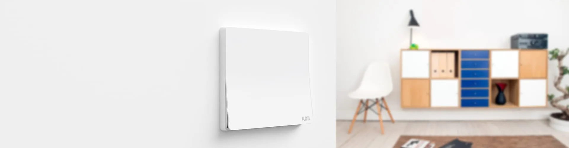 Weißer ABB XUAN ZHI Schalter an weißer Wand; verschwommenes Wohnzimmer mit Regalwand und Designstuhl dahinter