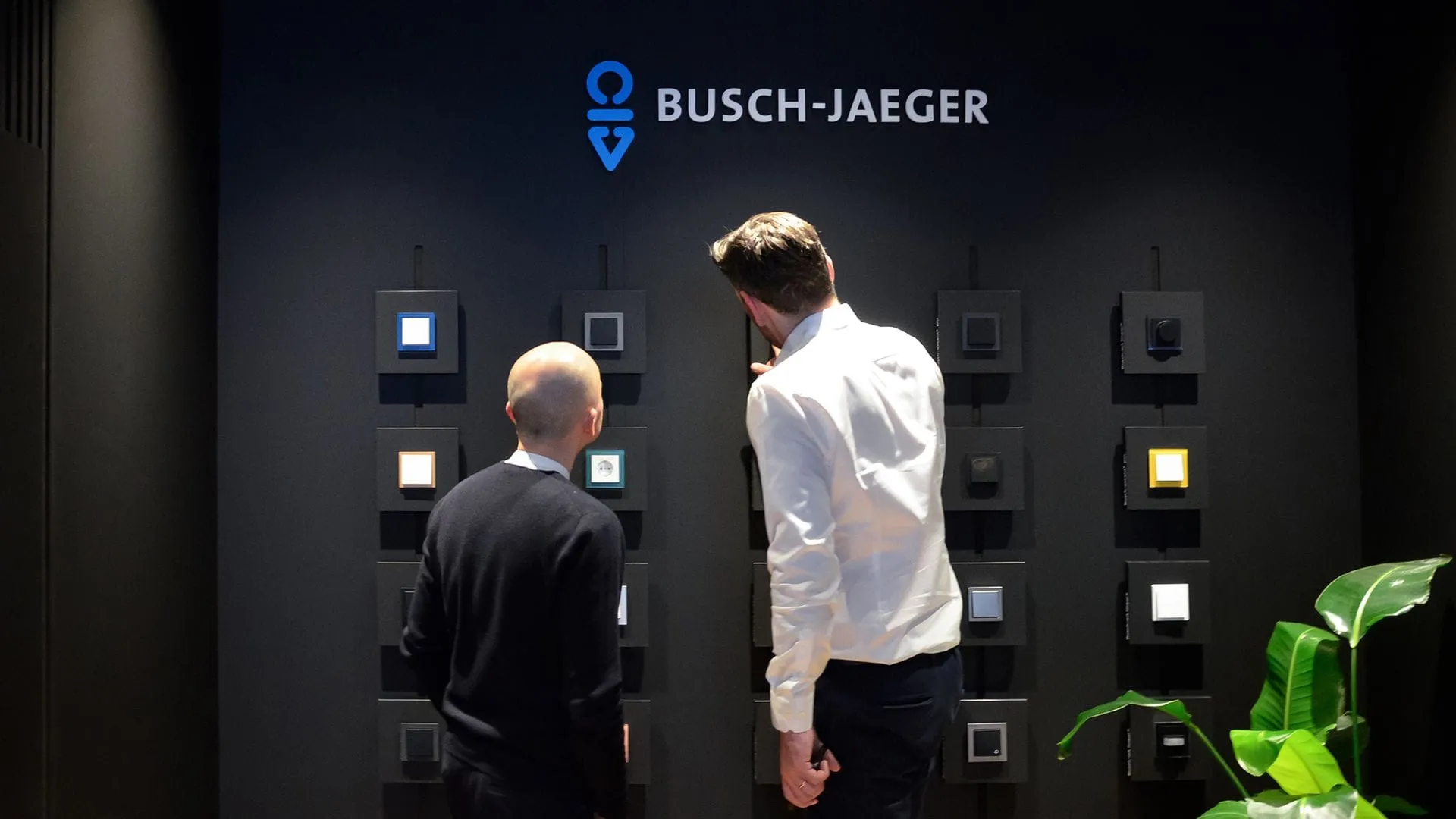 Zwei Besucher betrachten die Busch-Jaeger Showroom-Wand mit Busch-art linear Schaltern auf einer Fachmesse